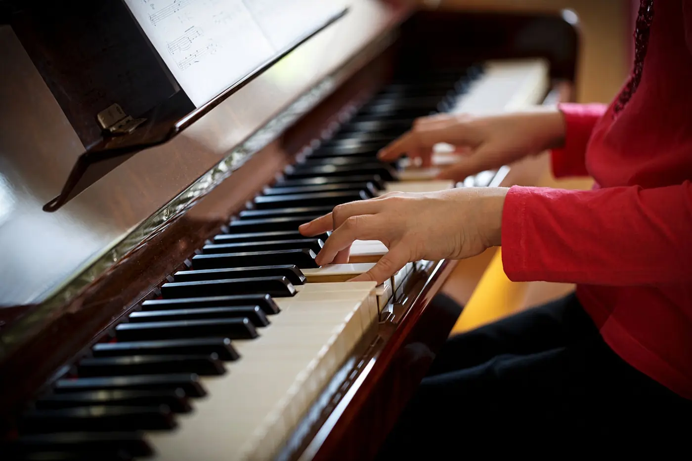 A young student's hands on the keys of a wooden upright piano